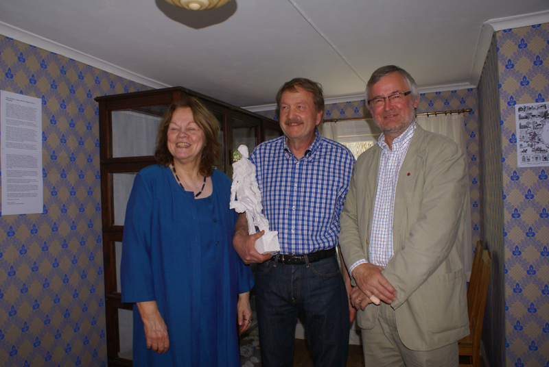 Aase Fridegård Penayo, Rune Rydelius och Mats O Karlsson framför skåpet i Lilla stugan där skisserna till statyn visas.